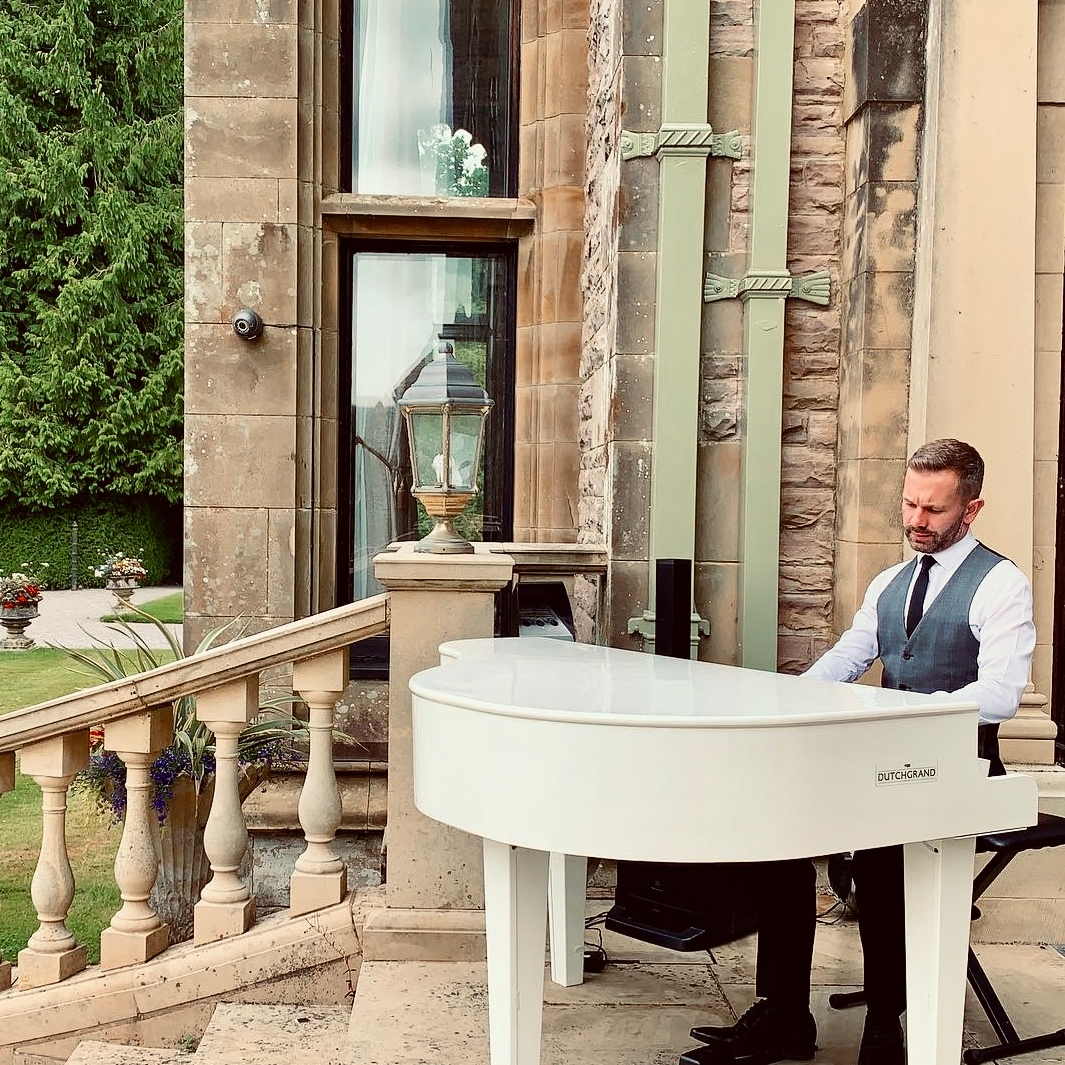 Armathwaite Hall wedding pianist Craig Smith performing on his white baby grand piano during a drinks reception outside on the terrace overlooking Bassenthwaite